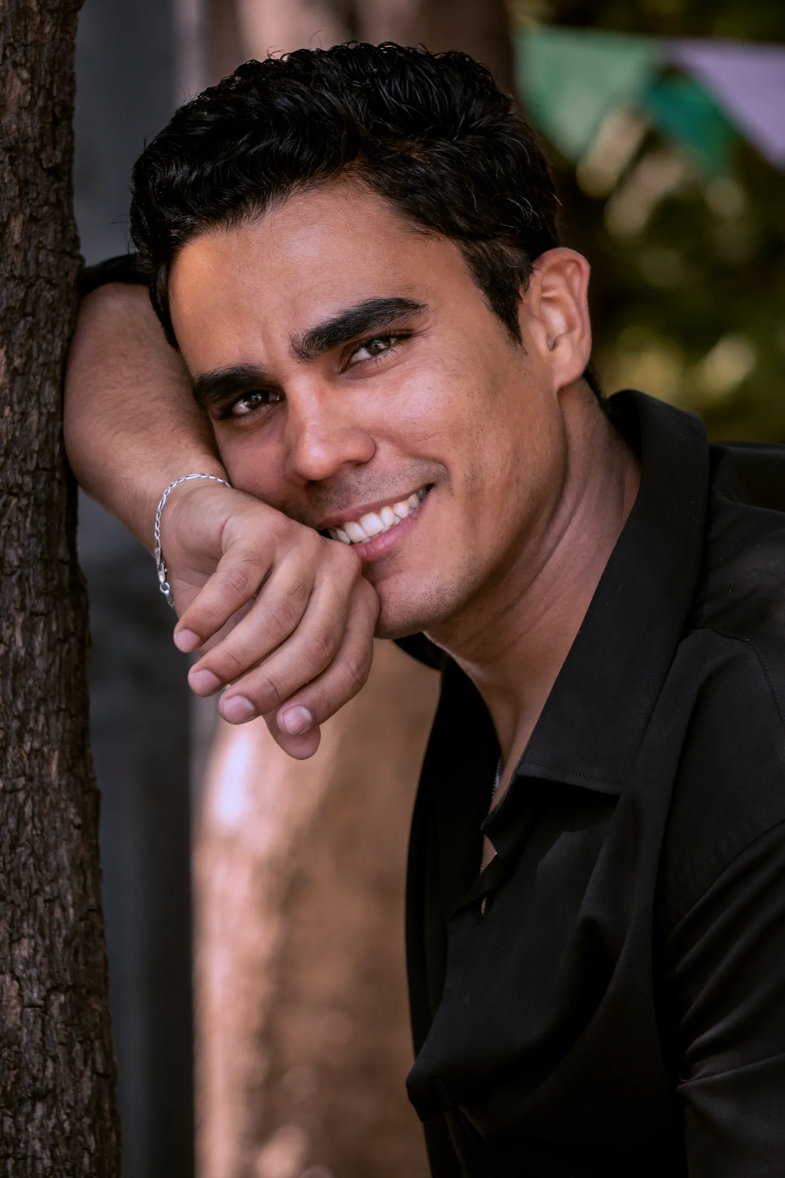 Retrato de hombre sonriendo recargado en un árbol